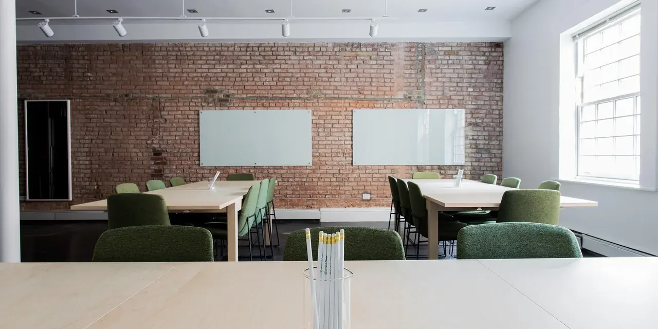 Salle de séminaire vide, tables disposées en îlots devant deux tableaux blancs
